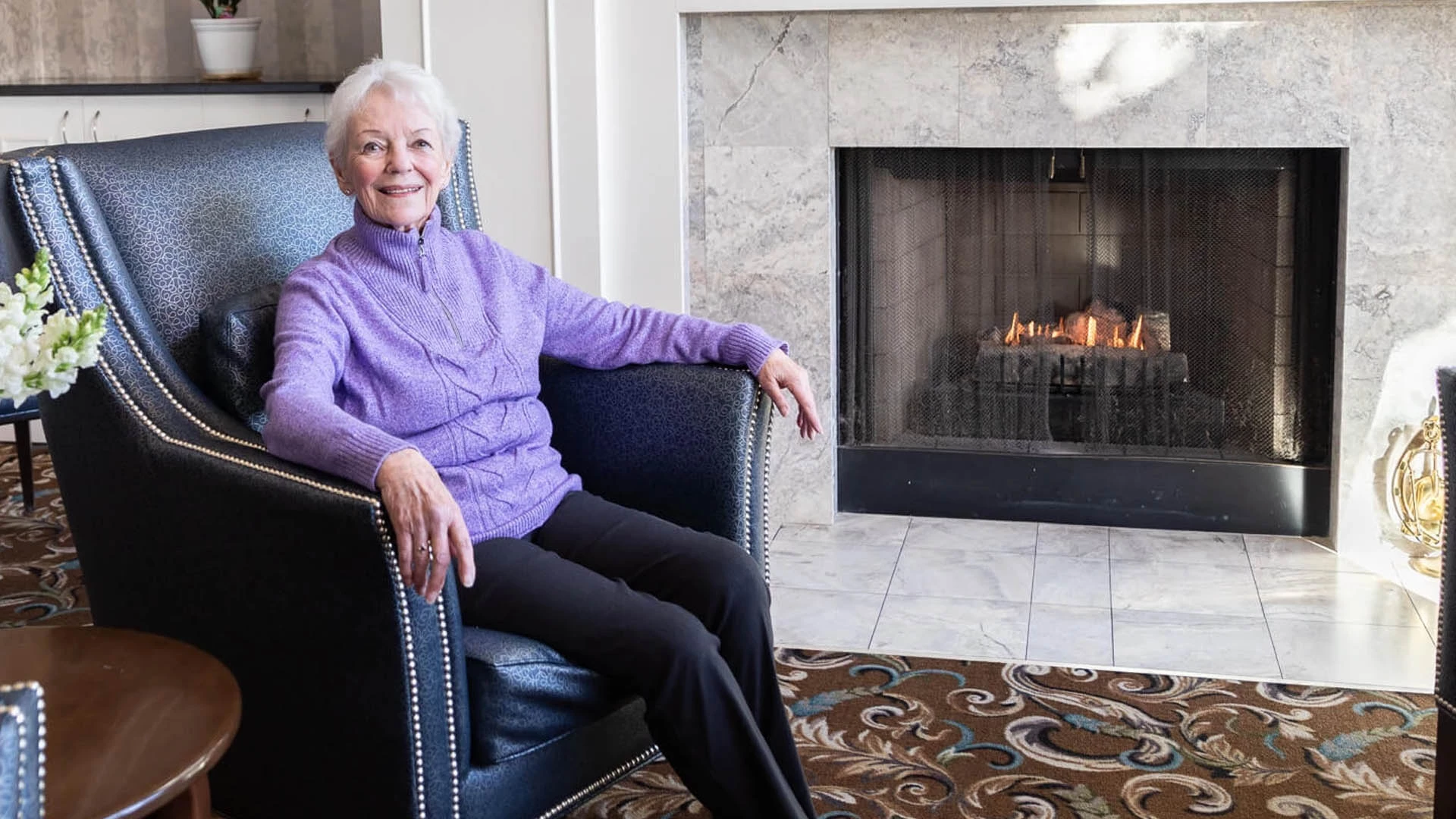 A woman sitting in a chair in front of a fireplace.