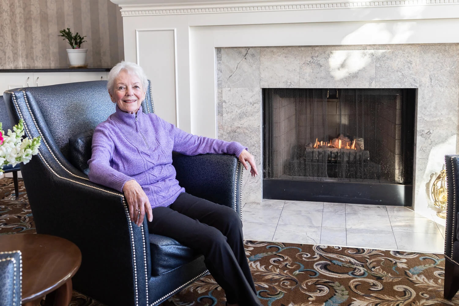 A woman sitting in a chair in front of a fireplace.