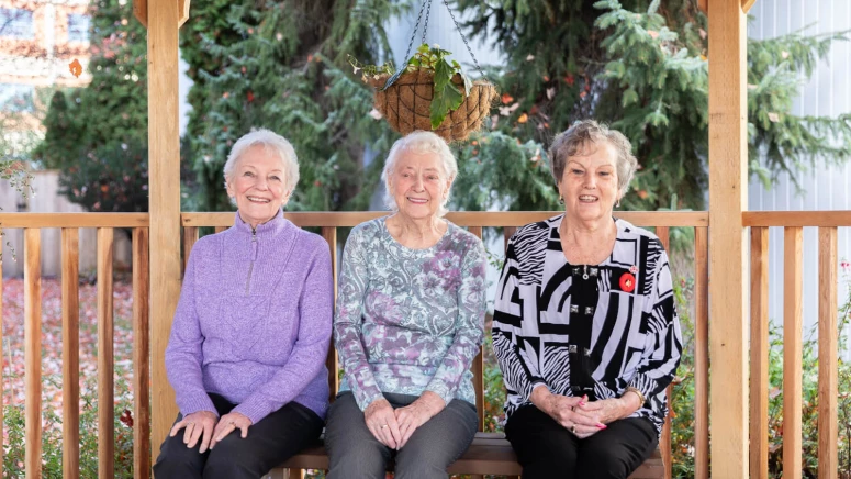 Three older women sitting on a wooden bench.